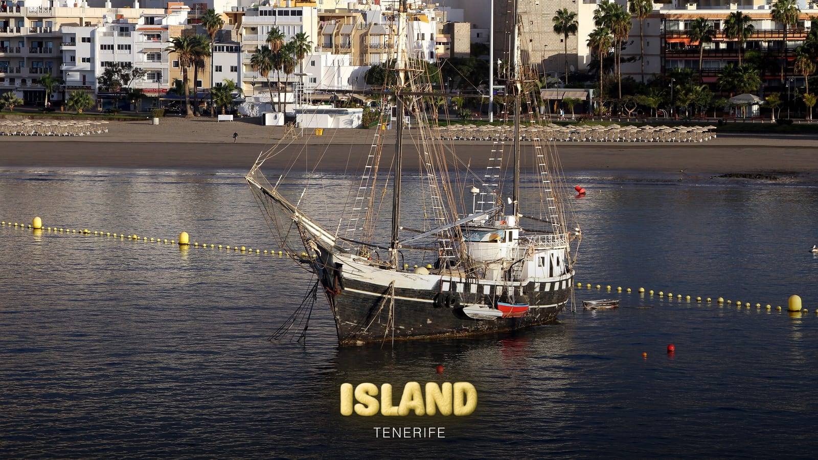 A two-masted sailing ship anchored off the beach at Los Cristianos