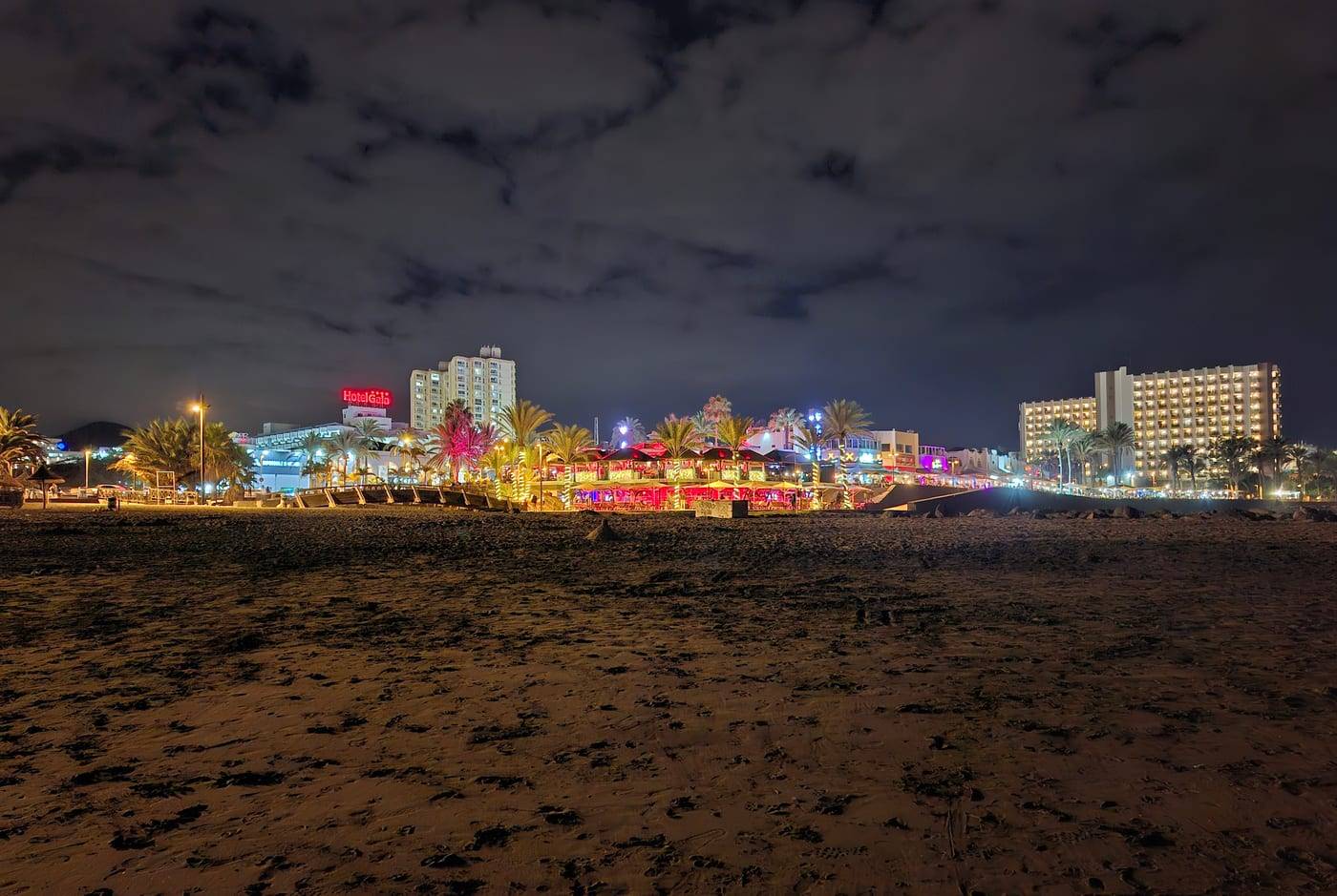 The lit-up strip of bars and hotels in Playa de las Américas at night, seen from the beach